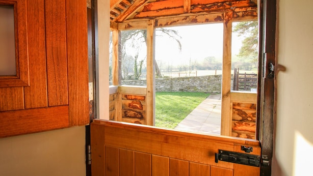A wooden door with a view of a stone wall and a grassy area outside.
