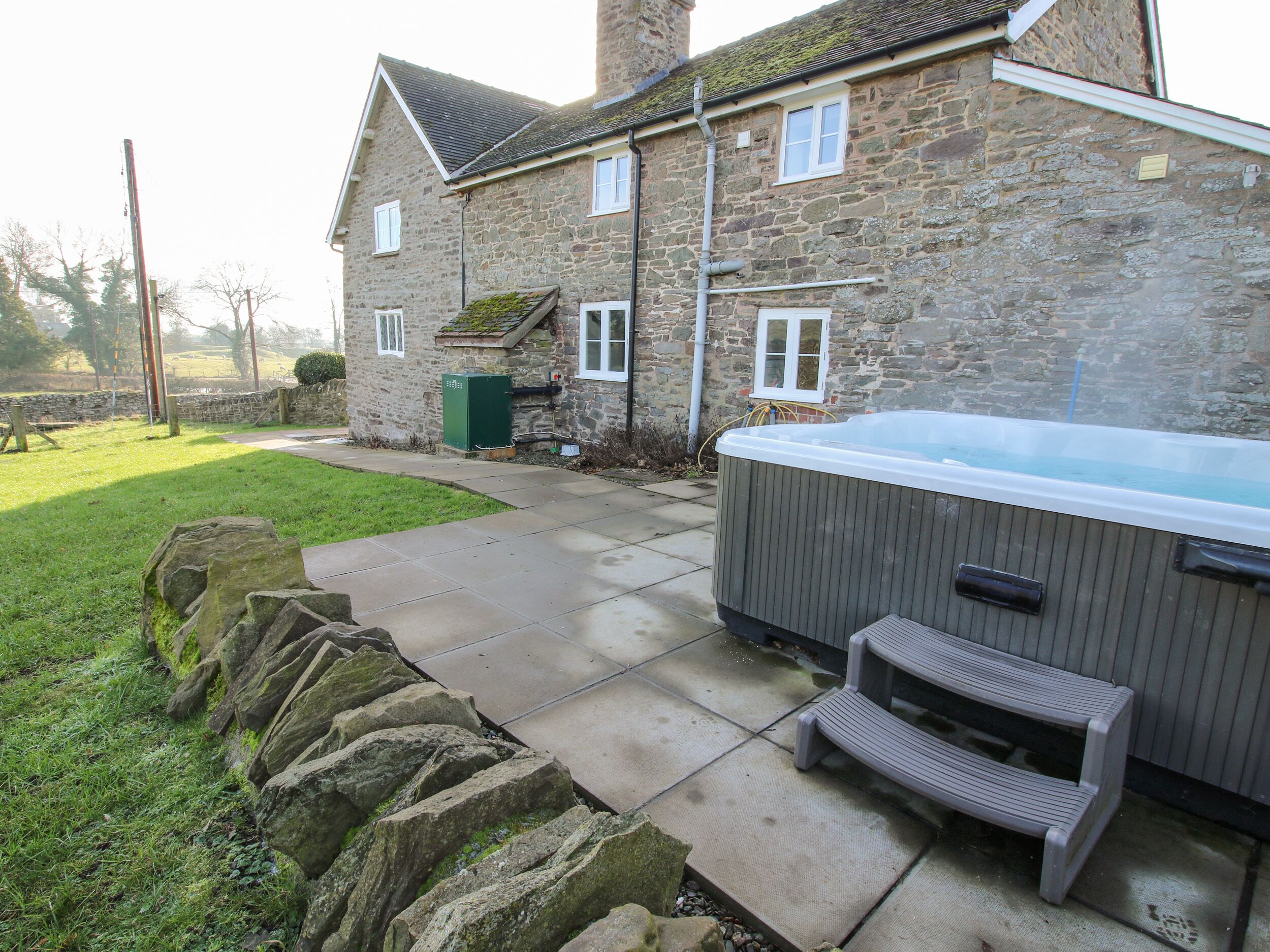 Une maison en pierre avec un jacuzzi et un petit escalier menant à une terrasse.