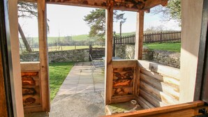 A rustic wooden structure with a stone wall and a view of a grassy field.