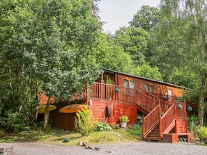 A rustic cabin with a wooden exterior, a staircase leading to a porch, and surrounded by dense forest. - Willow Lodge (Windermere)