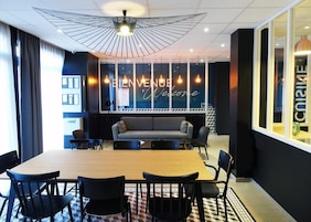 Une salle de réunion moderne, dotée d’une table en bois, de chaises noires, d’un canapé gris et d’un luminaire au plafond au design original.