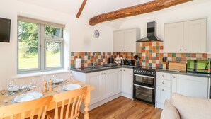 A kitchen with wooden beams, a tiled backsplash, and a dining area with a table set for four. - Sparrow Barn (Norwich)