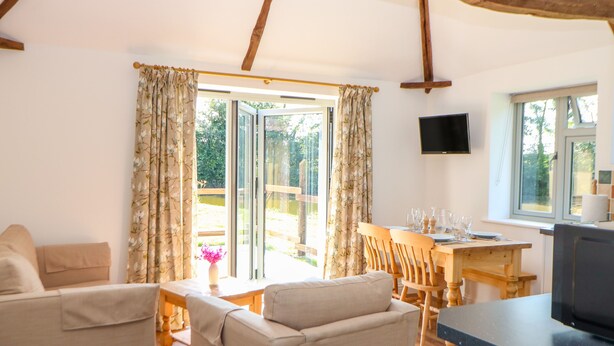 A cozy living room with a sofa, a dining table with chairs, and a TV mounted on the wall. - Sparrow Barn (Norwich)