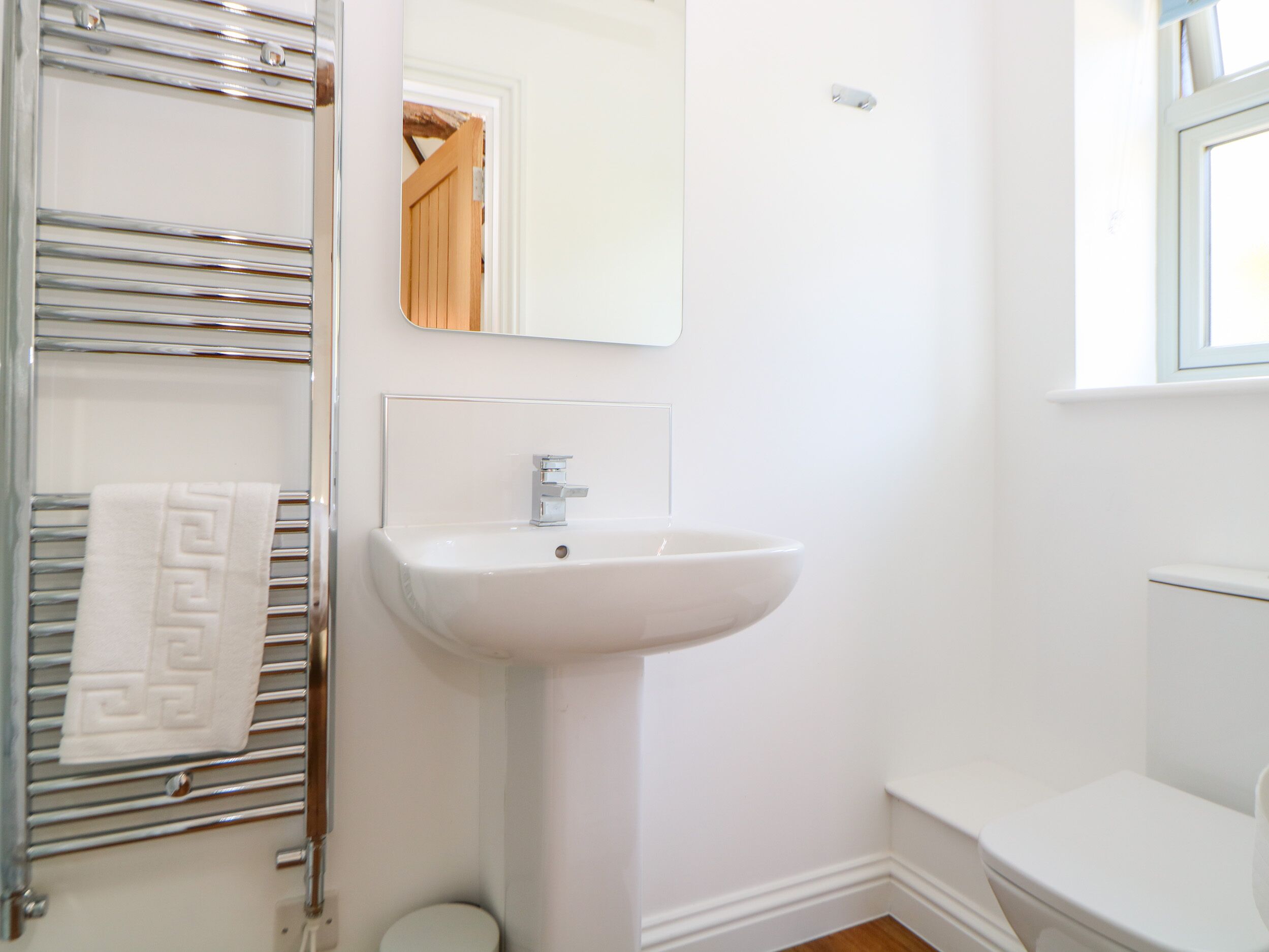 Ein Badezimmer mit einem weißen Waschbecken, einem Handtuchhalter mit einem gemusterten Handtuch, einem Spiegel und einer Toilette.