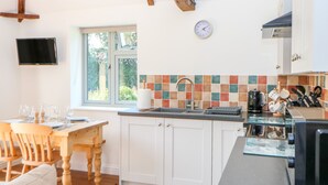 A kitchen with white cabinets, a tiled backsplash, a sink, and a window with a view of greenery. - Sparrow Barn (Norwich)