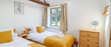 A bedroom with two beds, a wooden dresser, a mirror, and a window with curtains.