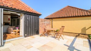 A patio with a table and chairs, a sliding door to a room, and a tiled roof. - Sparrow Barn (Norwich)