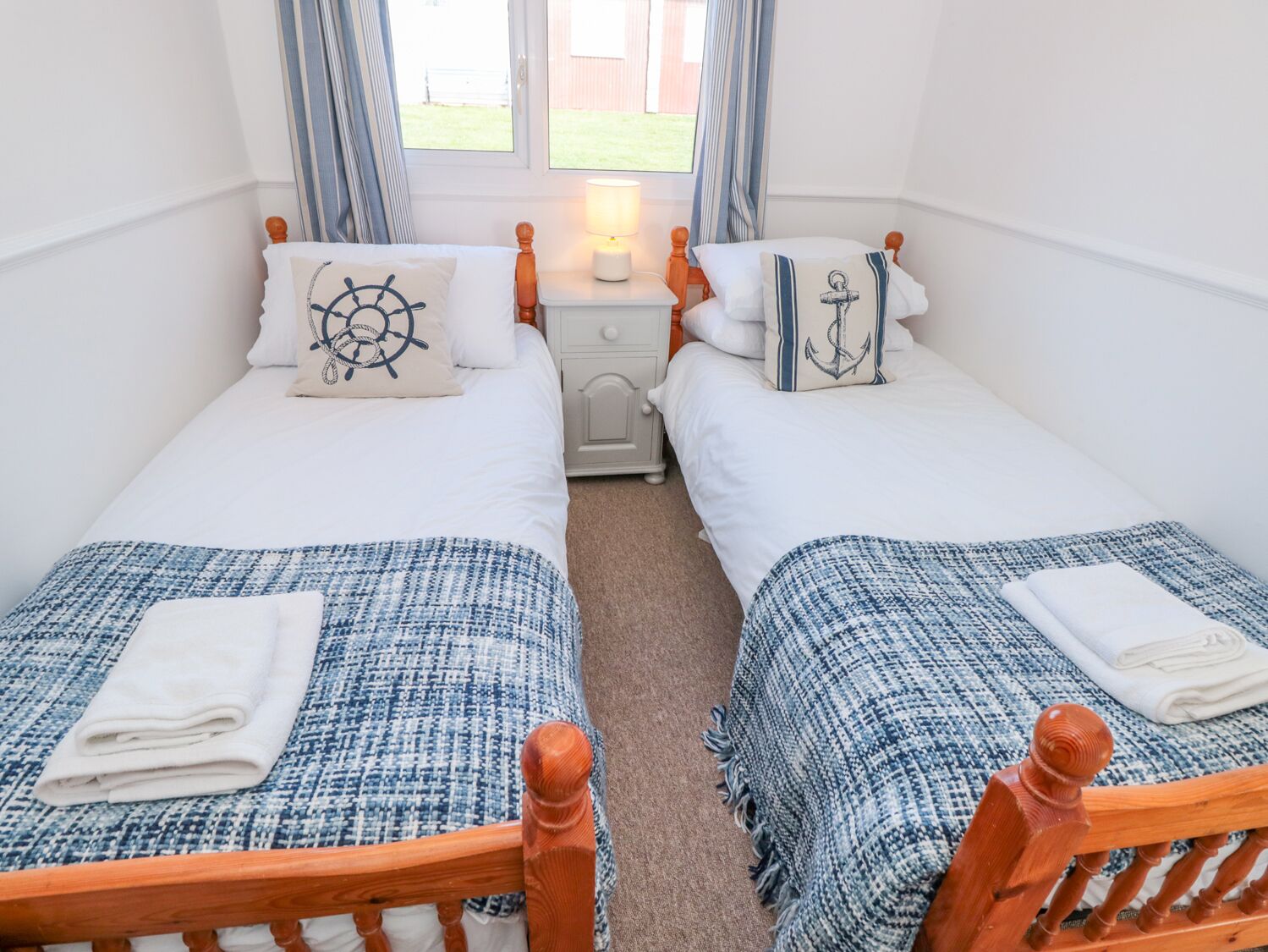 A twin room with two single beds, each with a matching headboard and footboard. There is a nightstand with a lamp between the beds, and a window with curtains.