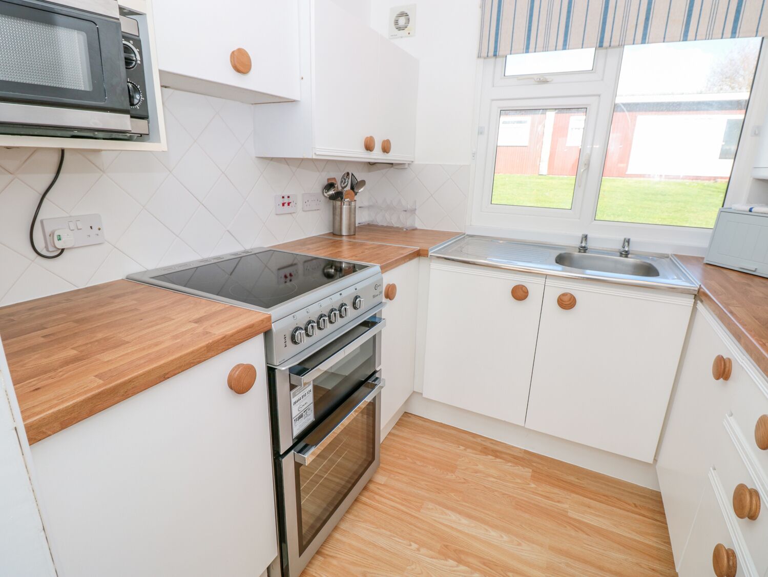 A compact kitchen with white cabinets, a built-in microwave, a stove, and a sink.
