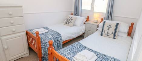 A bedroom with two single beds, a dresser, and a window with curtains.