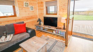 Interior acollidor d'una cabana amb decoració de fusta, un sofà, una televisió i una prestatgeria.