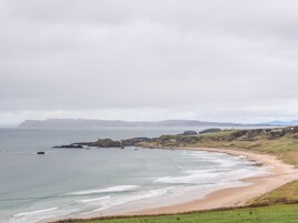 Un paisaje costero con una playa de arena, afloramientos rocosos y colinas cubiertas de hierba.