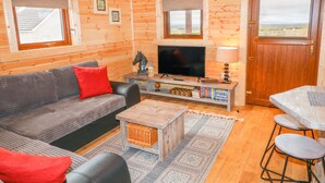 Interior acollidor d'una cabana amb elements de fusta, un sofà, una televisió i zona de menjador.