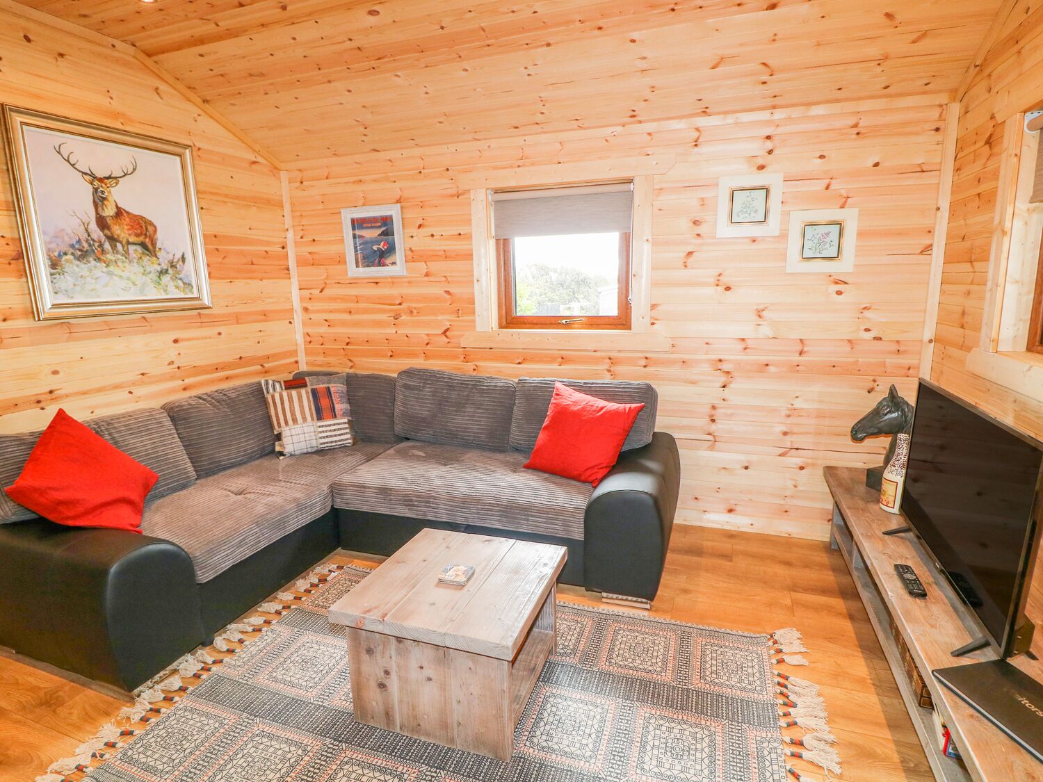 Interior acogedor de una cabaña con un sofá modular, una mesa de centro, un televisor y cuadros en las paredes.