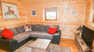 Interior acogedor de una cabaña con un sofá modular, una mesa de centro, un televisor y cuadros en las paredes.
