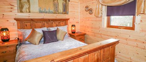 A wooden cabin bedroom with a bed, nightstands, and a window with curtains.
