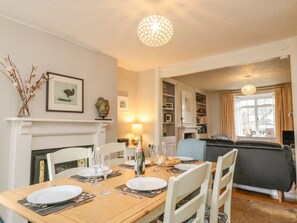 A dining area with a wooden table set for four, white chairs, a fireplace, and a bookshelf.