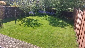 A well-maintained backyard with a wooden deck, a stone wall, and a variety of flowering plants. - Croft Cottage (Lancaster)