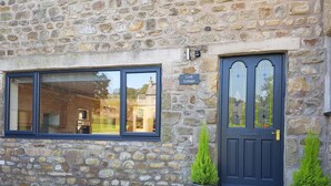A stone building with a dark blue door and windows, a sign reading "Croft Cottage," and two potted plants beside the door. - Croft Cottage (Lancaster)