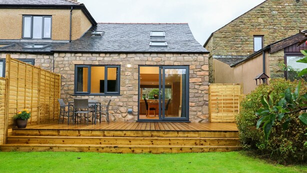 A stone house with a wooden deck, a dining area, and a large glass door leading to an interior space. - Croft Cottage (Lancaster)