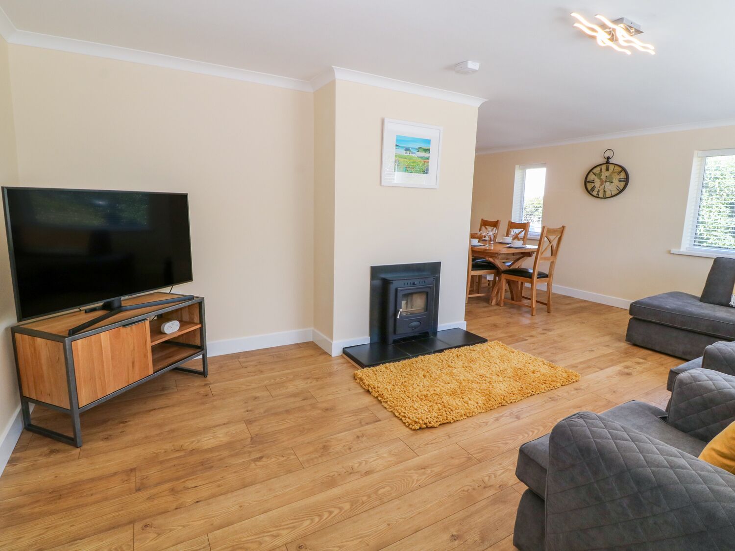Een woonkamer met een flatscreen televisie, een open haard, een bank en een eethoek met houten meubels.