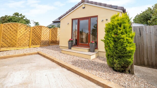 A small, single-story building with a beige exterior, a wooden door, and a small porch area. - Eastdown Annexe (Totnes)