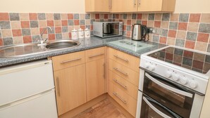 A kitchen with wooden cabinets, a stainless steel sink, a microwave, a kettle, and a stove. - Eastdown Annexe (Totnes)