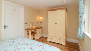 A bedroom with a bed, a desk, a wardrobe, and a window with a curtain. - Eastdown Annexe (Totnes)