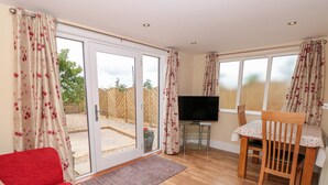 A living room with a red sofa, a wooden chair, a TV on a stand, and a sliding glass door leading to an outdoor area. - Eastdown Annexe (Totnes)