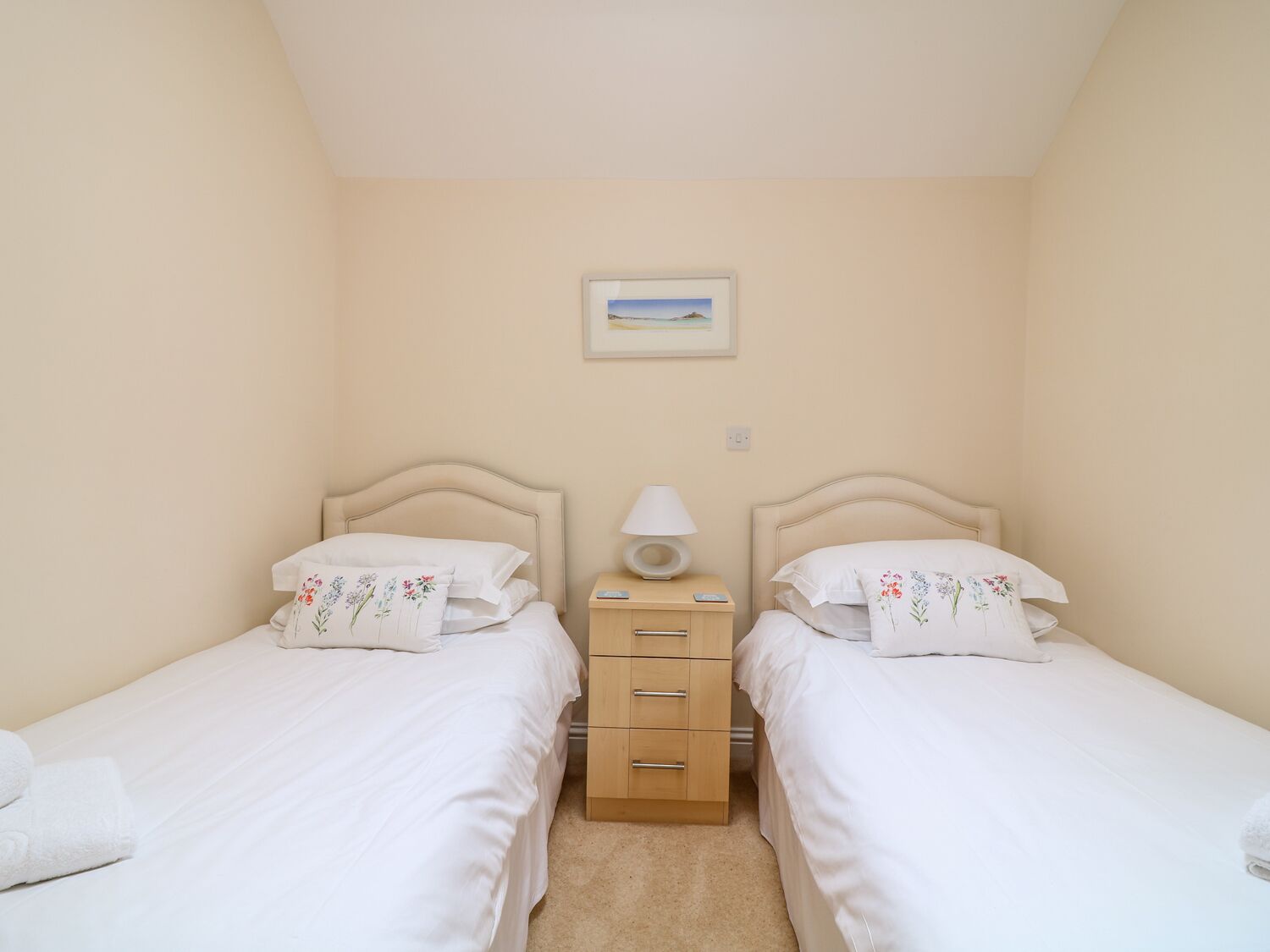A twin bedroom with two beds, a bedside table with a lamp, and a small cabinet.