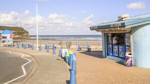 Eine Küstenstraße mit einem Eiscafe direkt am Strand, einem Wegweiser und einer Fahnenstange.