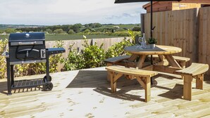 An outdoor deck with a barbecue grill, wooden table, benches, and an umbrella. - Sea Dreams (Marazion)