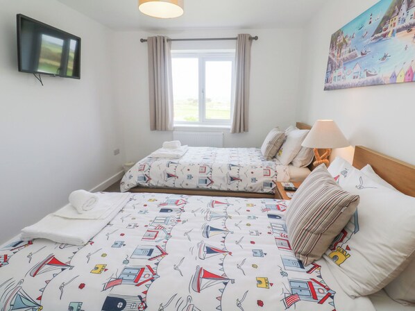 A hotel room with two beds, a television, a window with curtains, and a painting on the wall. - Sea Dreams (Marazion)