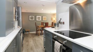 Een moderne keuken met roestvrijstalen apparatuur, een eethoek met een tafel en stoelen, en een klein krukje.