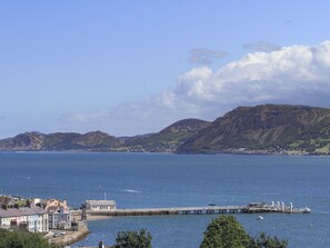 Un pueblo costero con un muelle que se adentra en el mar, rodeado de colinas y un cielo despejado.