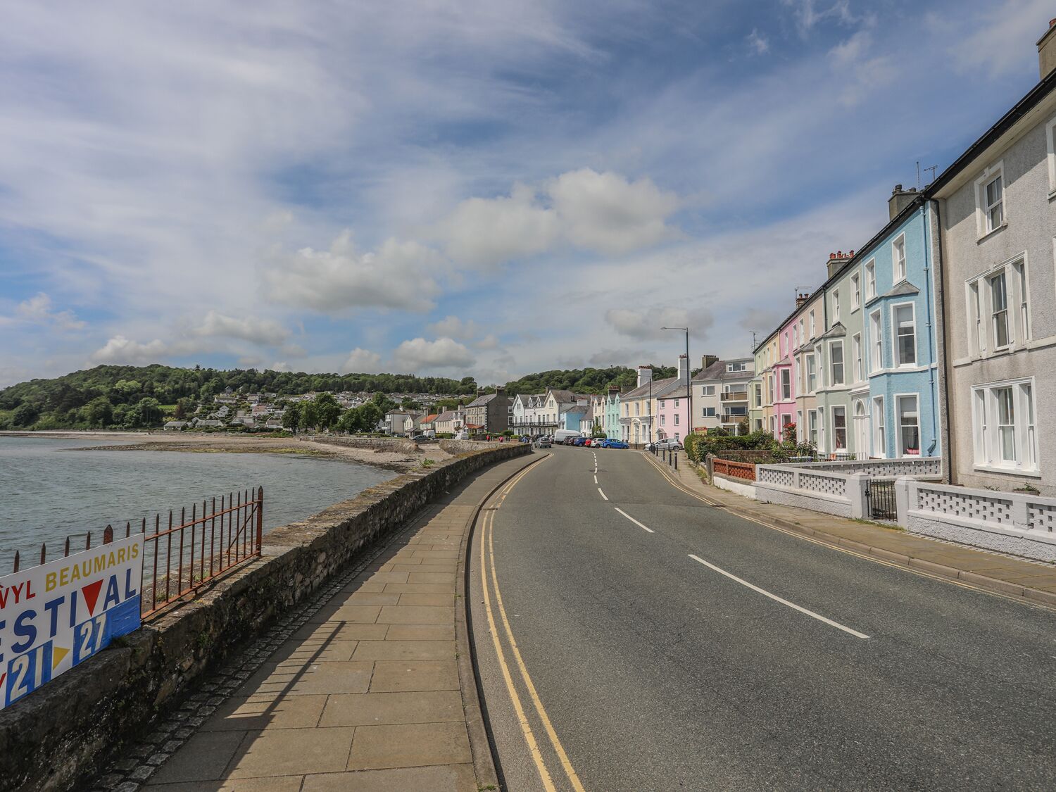 A coastal road with colorful houses on one side and a sea view on the other.
