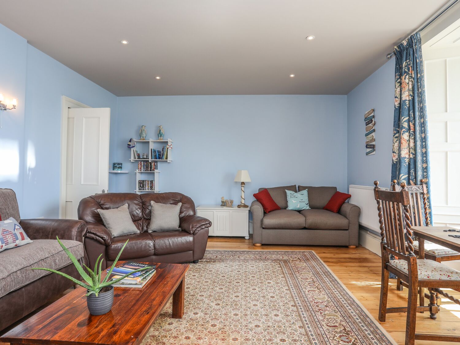 Ein Wohnzimmer mit zwei Sofas, einem Couchtisch mit einer Pflanze, einem Bücherregal und einem Essbereich mit einem Stuhl.