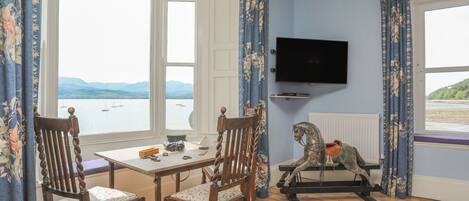 A room with a table and chairs, a television, a rocking horse, and a view of the sea.