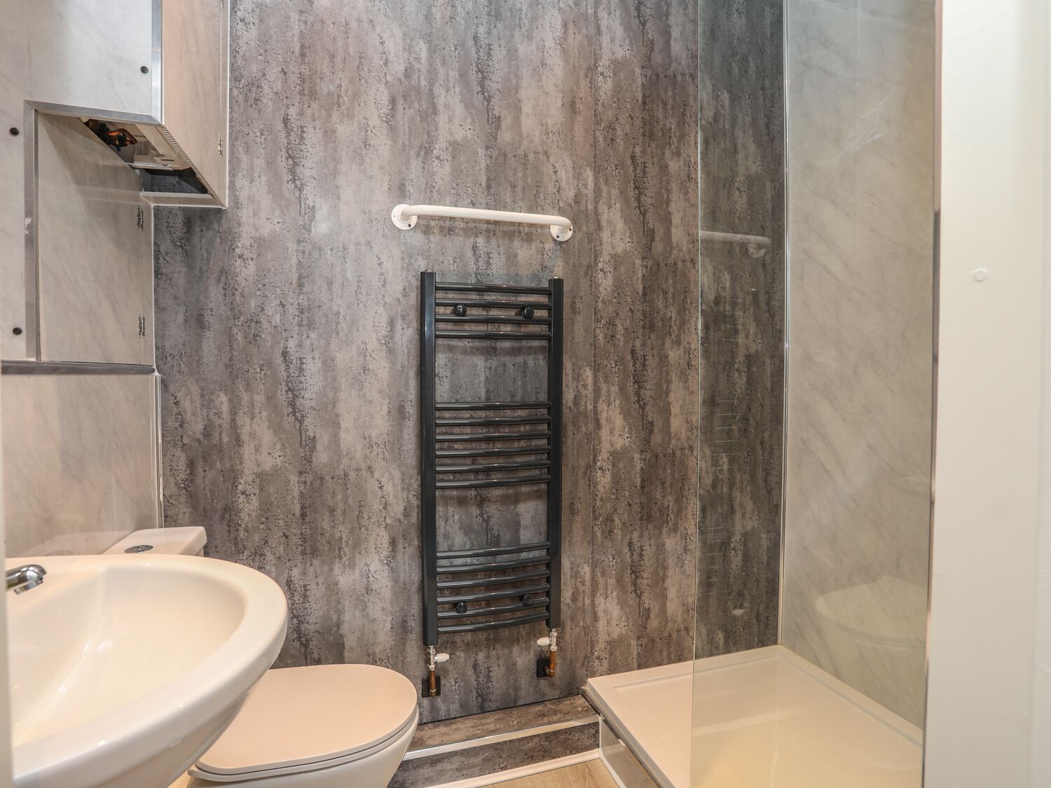 A bathroom with a white sink, toilet, and bathtub, a towel rack, and a shower with a glass door.