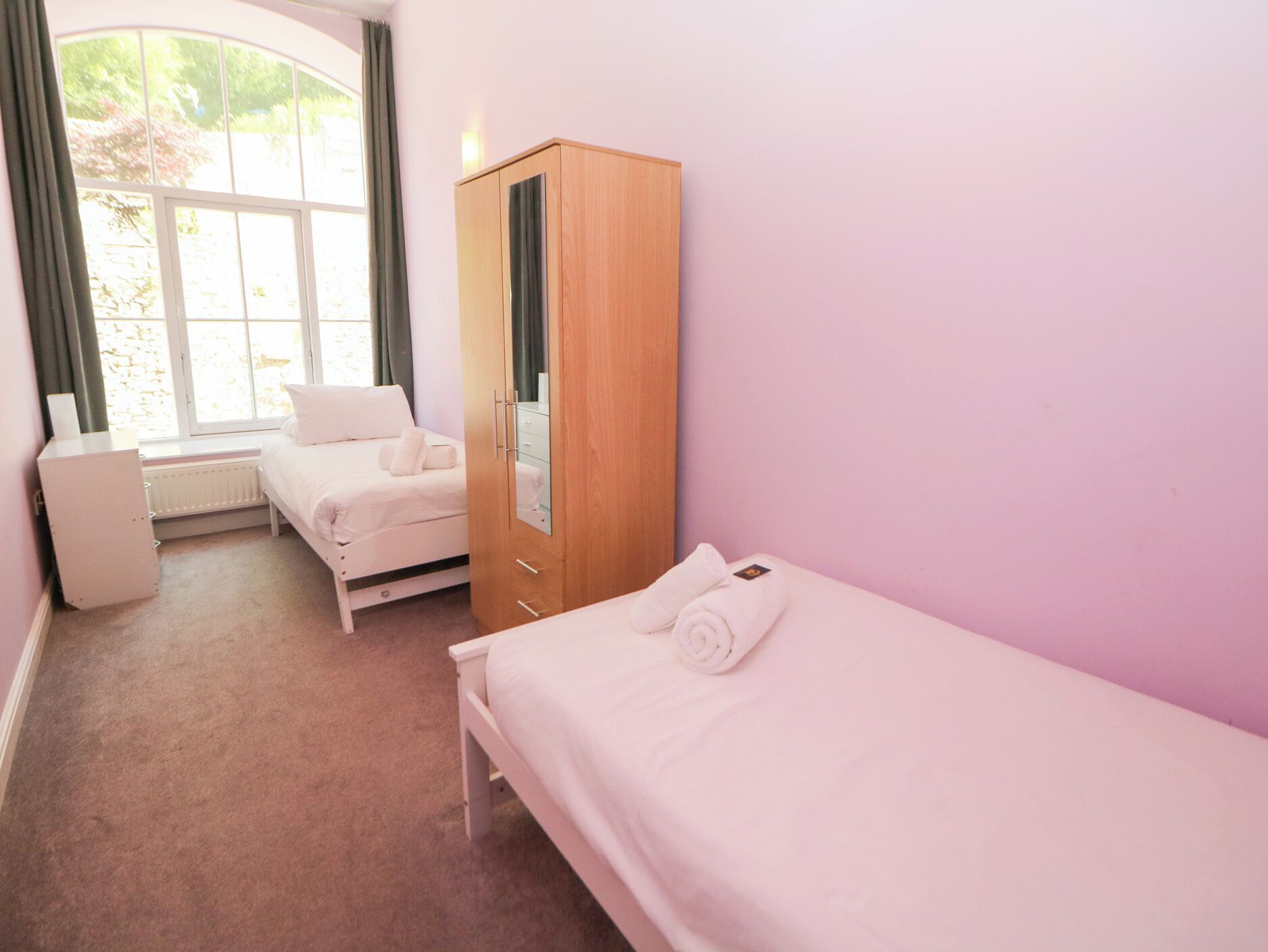 Ein Schlafzimmer mit Bett, Kleiderschrank, Heizkörper und einem Fenster mit Vorhängen.