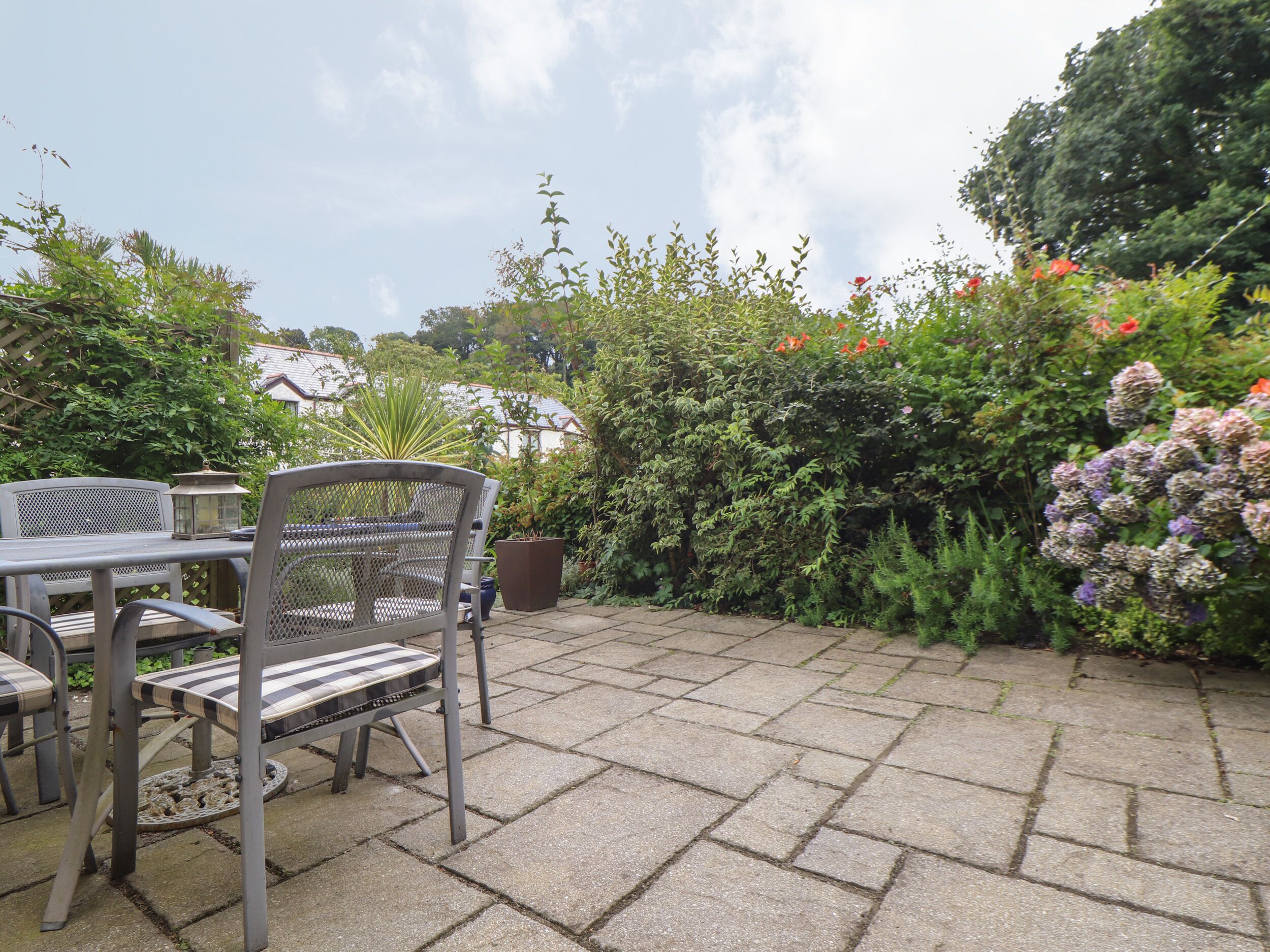 An outdoor patio with a table and chairs, surrounded by lush greenery and flowering plants.