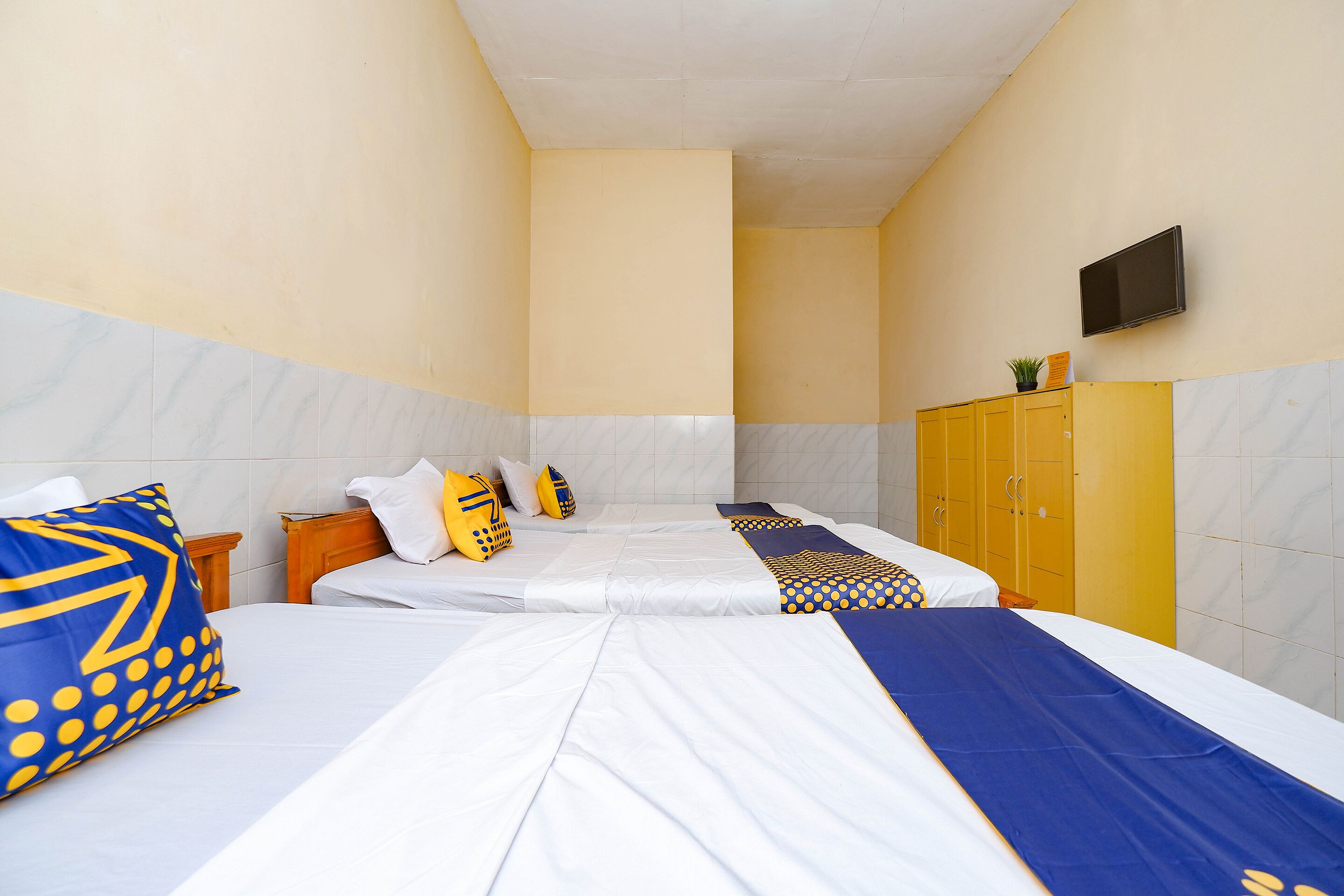 A hotel room with two beds, a television on the wall, and a wardrobe.