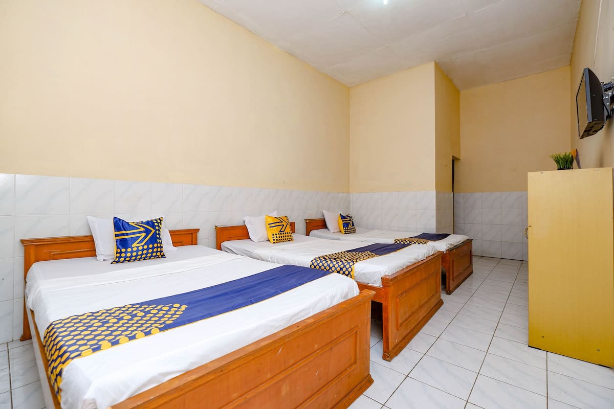 A hotel room with three wooden beds, each with white bedding and blue and yellow patterned bedspreads.