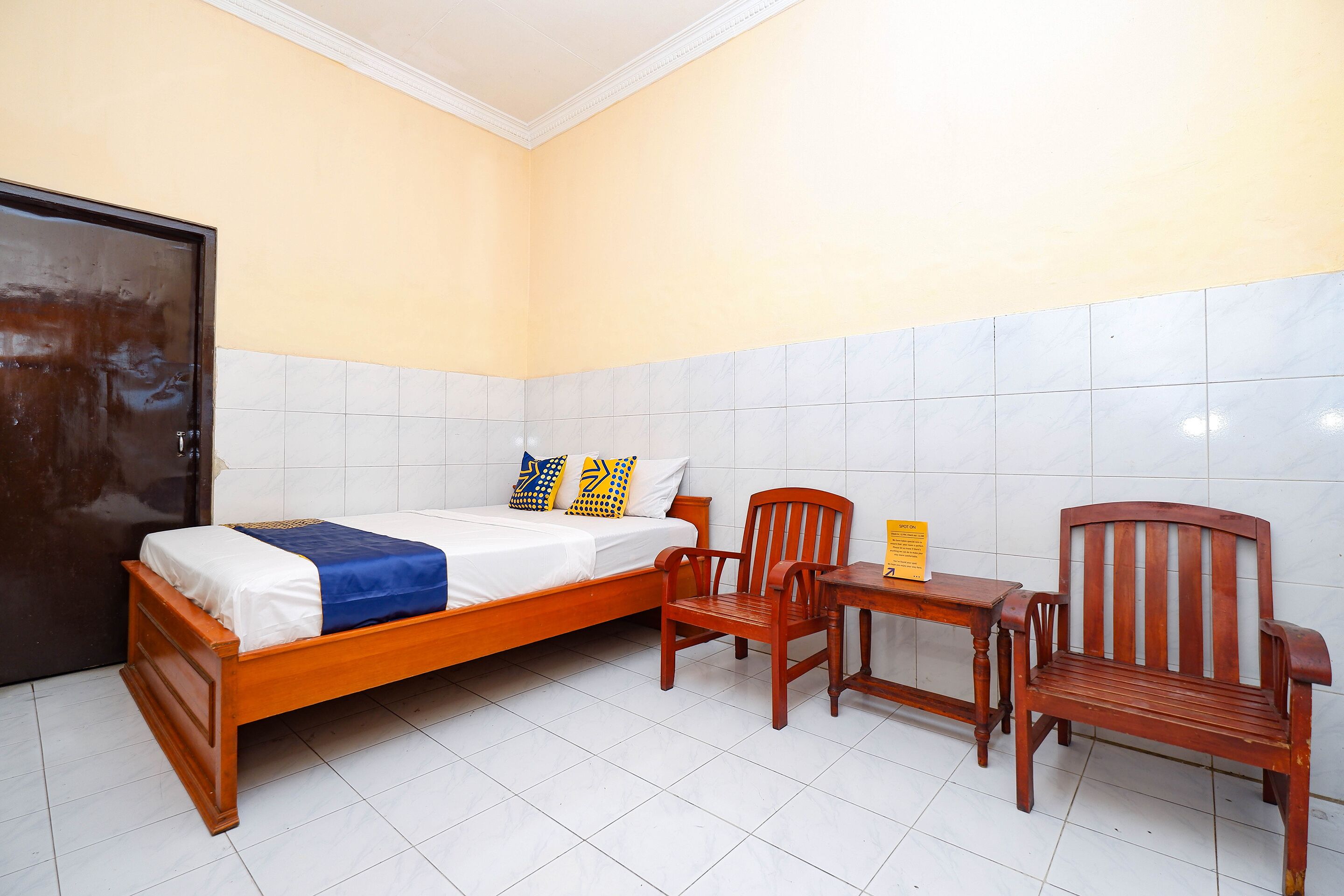 Ein Schlafzimmer mit einem hölzernen Bett, zwei Stühlen, einem kleinen Tisch und einer Tür.