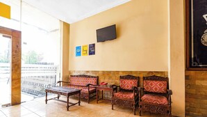 A lobby with a tiled floor, a sofa set, a wooden table, a flat-screen TV mounted on the wall, and a stone wall. - SPOT ON 2011 Hotel Mekar Sari (Surakarta)