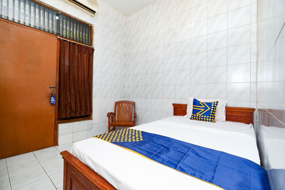 A hotel room with a bed, wooden headboard, a chair, and a window with curtains.
