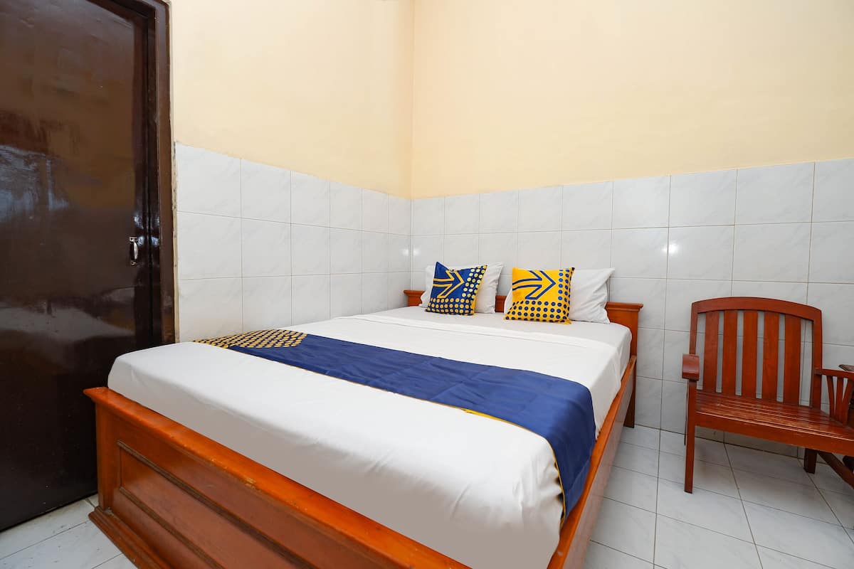 A neatly made bed with a blue and white bedspread, two pillows with geometric patterns, and a wooden chair beside the bed.