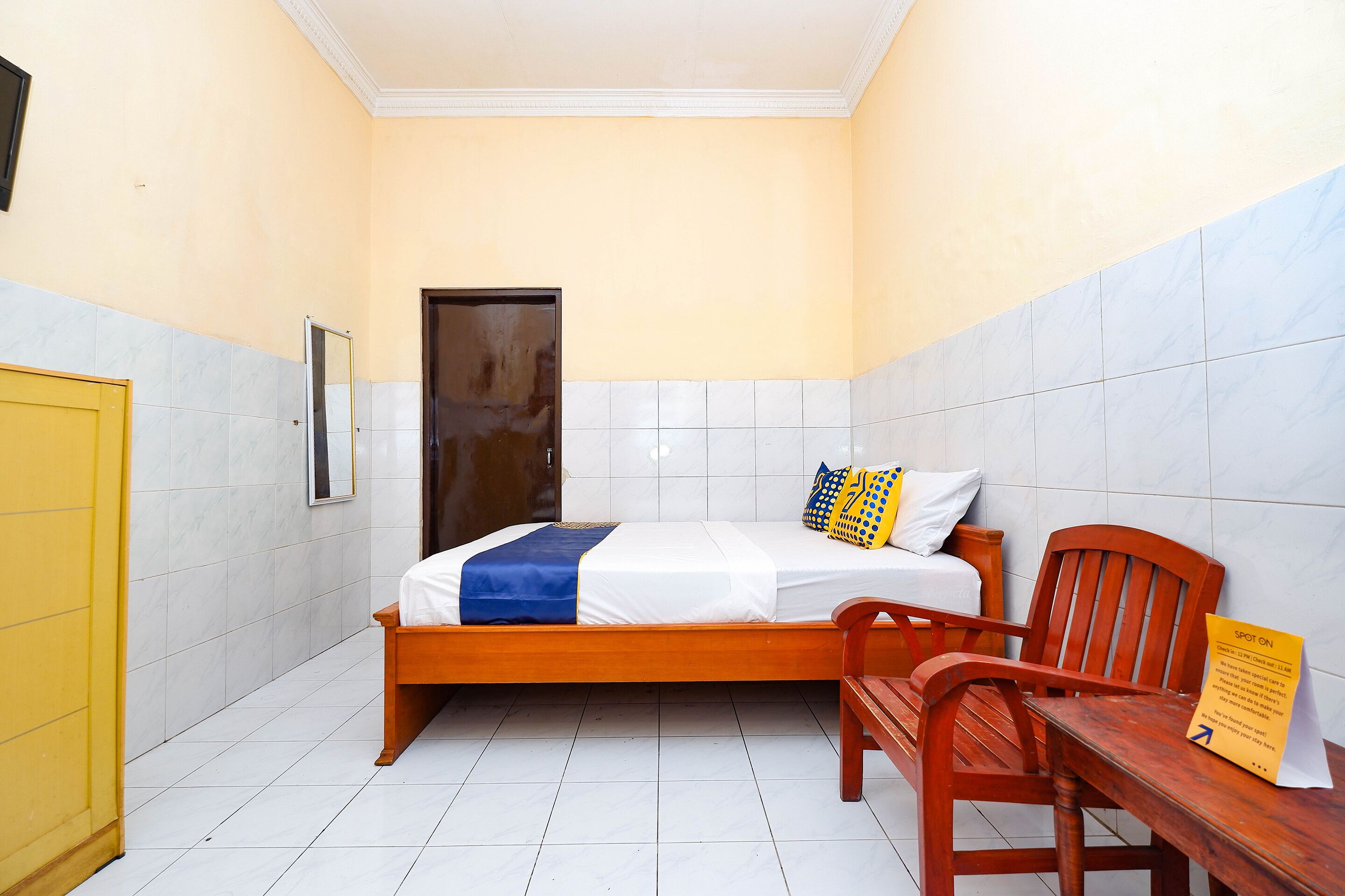 Une petite chambre d’hôtel, de taille réduite, avec un lit simple, un banc en bois et une petite table.