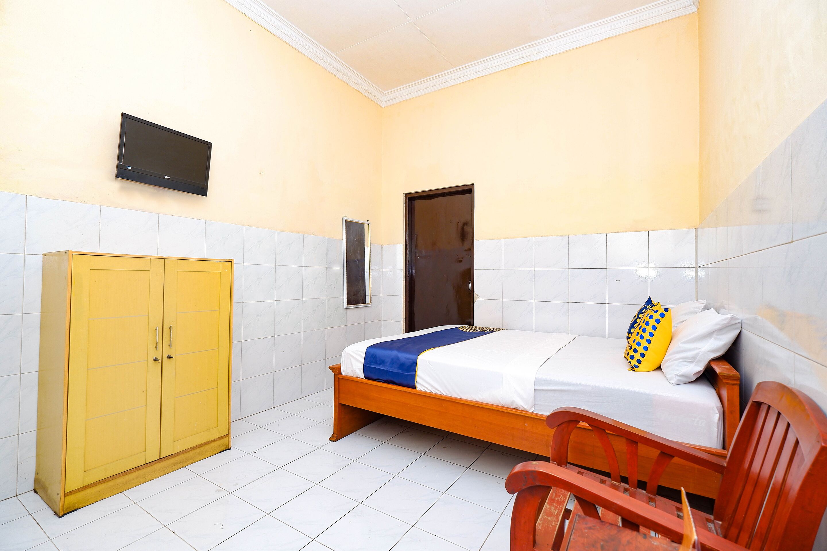 A bedroom with a bed, a wooden wardrobe, a television, and a door.