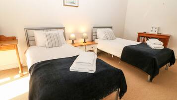 Ett hotellrum med två sängar, ett nattduksbord med lampor, ett litet träbord och en bokhylla.